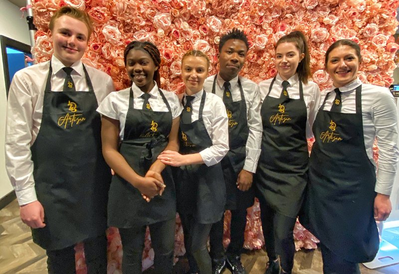 An image of six Little Dessert Shop staff in the Reading restaurant stood in front of a floral back drop